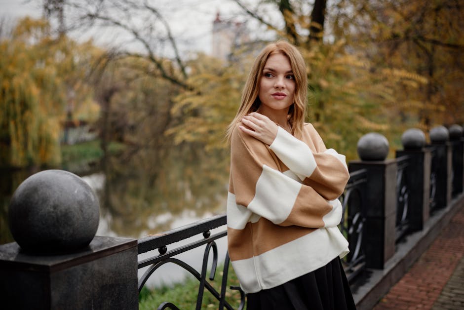 Fashionable woman standing by a park railing in autumn, showcasing style with arms crossed.