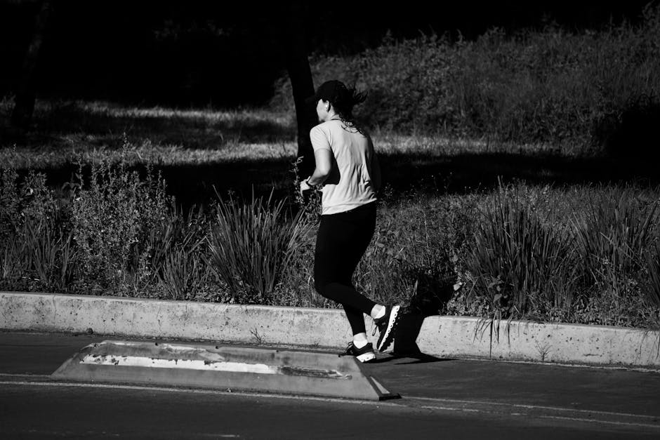 Black and white image of a woman jogging on a sidewalk, capturing motion and shadow.