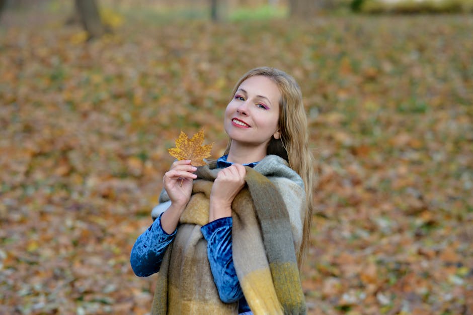 Smiling woman holds a maple leaf surrounded by autumn foliage, exuding warmth and seasonal joy.