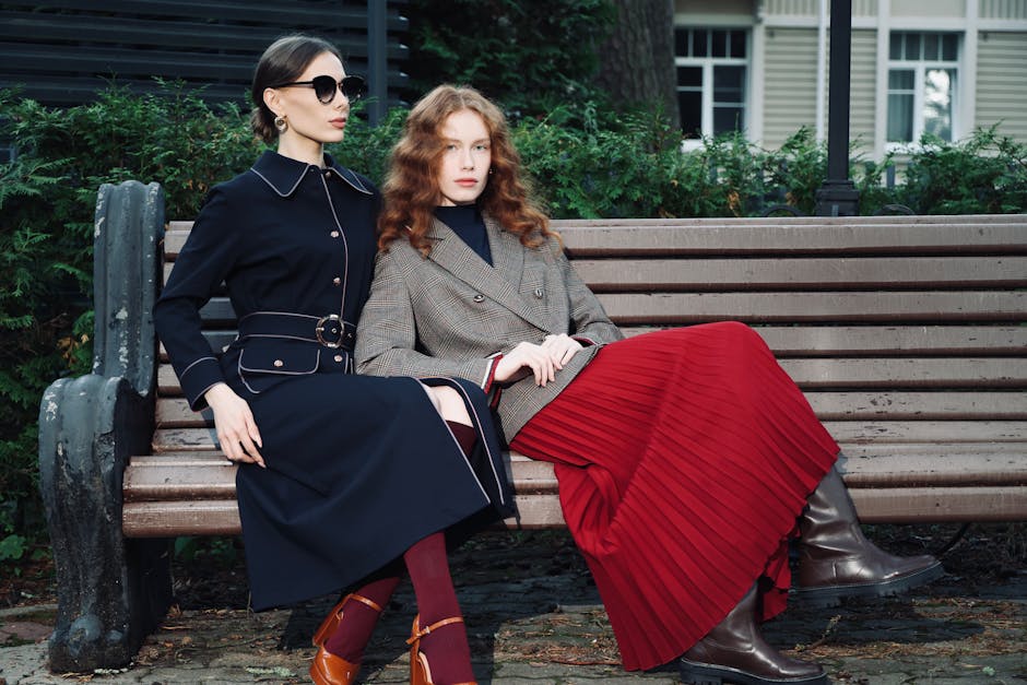 Two women in stylish fall outfits seated on a park bench, exuding elegance and sophistication.