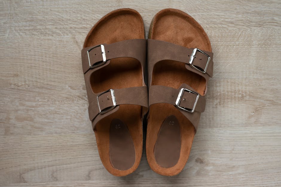Close-up of stylish brown leather sandals with silver buckles on wooden floor.