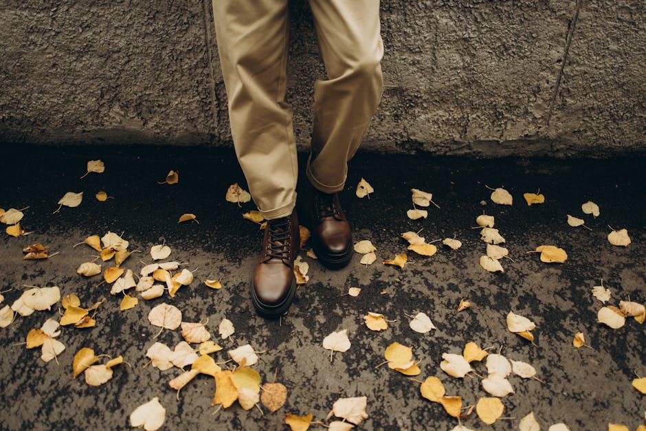 Close-up of leather boots and khaki pants amidst fallen autumn leaves.
