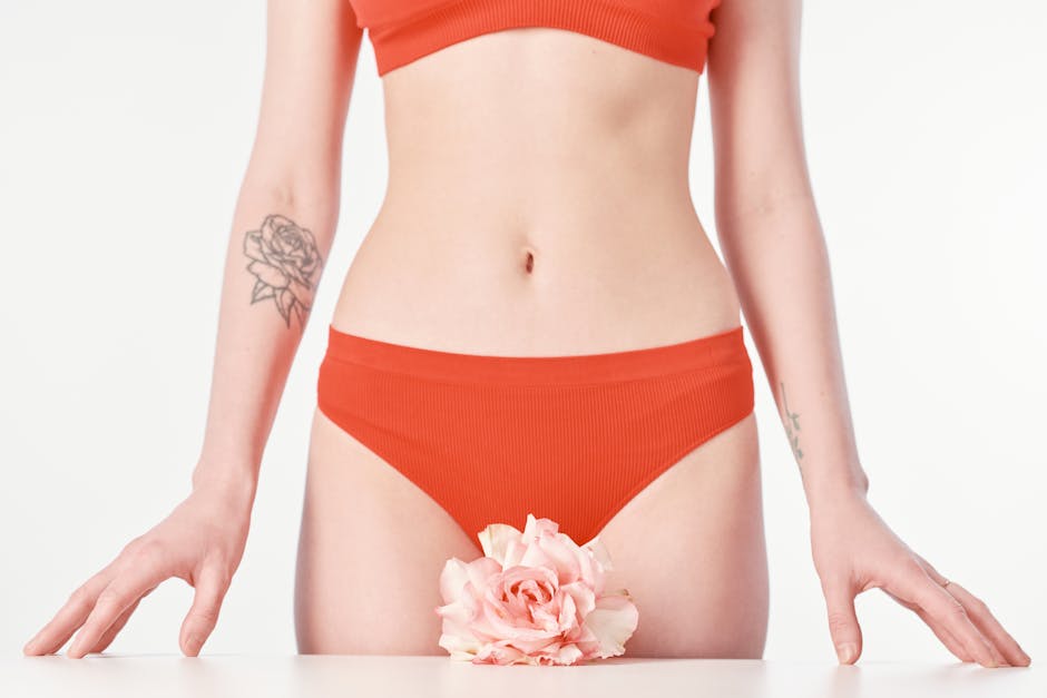 Close-up of a woman's midsection showcasing tattoos, floral element, and vibrant orange underwear.